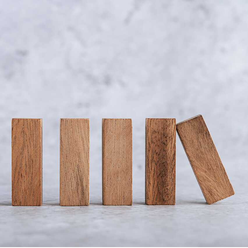Fünf stehende Holzklötze auf hellem Untergrund, einer kippt zur Seite