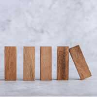 Fünf stehende Holzklötze auf hellem Untergrund, einer kippt zur Seite